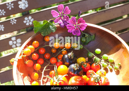 Creative variety of heirloom tomatoes in a rustic bowl and on a light wood surface Stock Photo