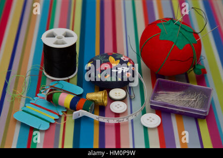 Colourful sewing kit on striped background pins cotton tape measure buttons Stock Photo