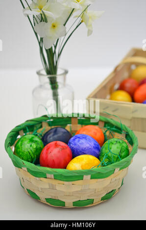 colorful Easter  eggs in a basket with white flowers on white background, close up, vertical Stock Photo