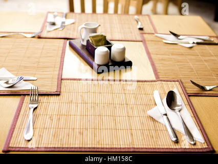 Table appointments- fork,knife,spoon, silk napkin on  bamboo mat Stock Photo