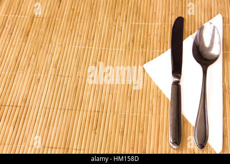 Table appointments- fork,knife,spoon, silk napkin on  bamboo mat Stock Photo
