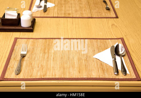 Table appointments- fork,knife,spoon, silk napkin on  bamboo mat Stock Photo