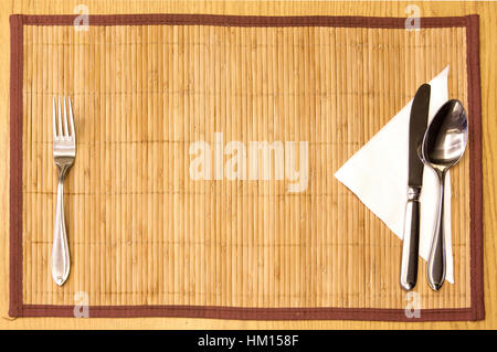 Table appointments- fork,knife,spoon, silk napkin on  bamboo mat Stock Photo