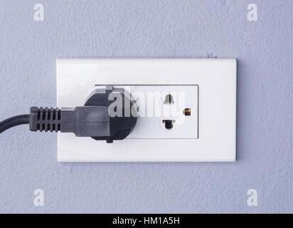 black cable plugged in a white electric outlet mounted on gray wall background Stock Photo