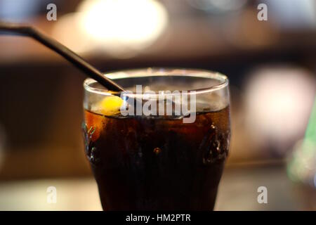 Coca Cola glass closeup. With a slice of lemon, ice cubes, and a black straw. Stock Photo
