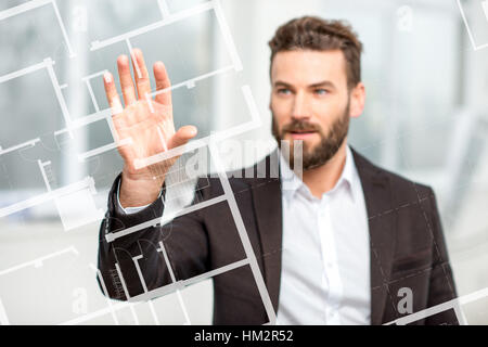 Architect or designer working with plan drawing on the virtual screen standing in the white room Stock Photo