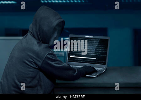 Hacker man wearing mask using laptop to upload computer virus in the office Stock Photo