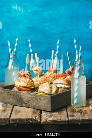 Different homemade burgers with sticks in wooden tray and lemonade Stock Photo