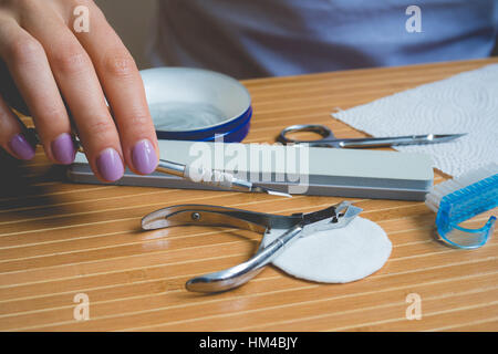 Manicure set on a wooden table. Female hand with colorful nails holding manicure tools. Retro picture. Stock Photo