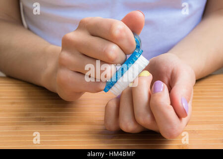 Female hands holding a nail brush. A young girl sits at a table and prepares manicure nail brush closeup. Stock Photo