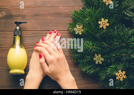 Female hands with red manicure and a bottle of hand cream on a wooden table. View from above. Stock Photo