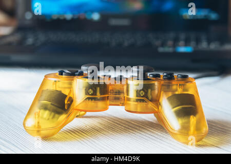 Yellow transparent joystick and a laptop with a video game on a table Stock Photo