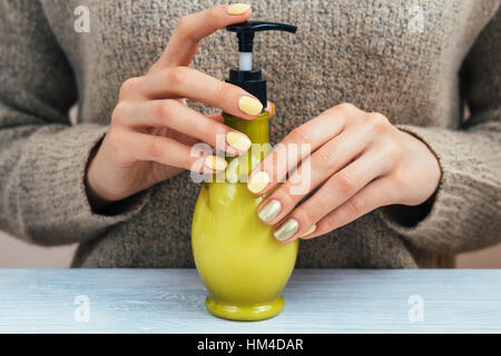 Female hand with bright manicure holding green bottle with cosmetic cream Stock Photo