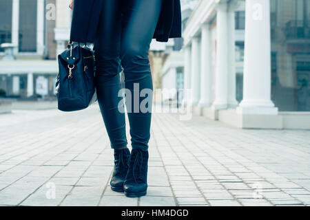 Details of women's clothing. Closeup of female legs in black pants and boots. Woman walking in the city, low-angle shooting, cold toning. Stock Photo