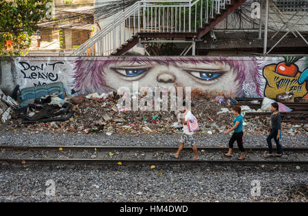 Graffiti looks over people walking along a railway line Stock Photo