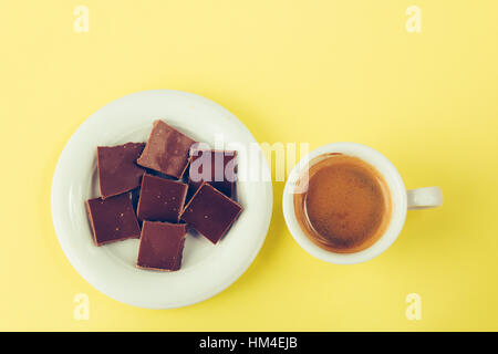 Chocolate on a saucer and a cup of coffee on a yellow surface, top view Stock Photo