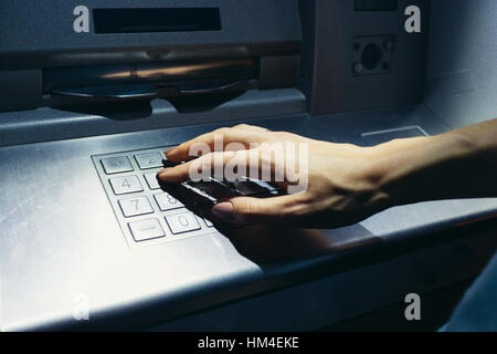 Woman's hand enters the secret code at the ATM on the street at night Stock Photo