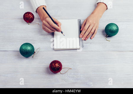 Woman writes in a notebook with a pencil, next on the table are Christmas tree balls, top view Stock Photo