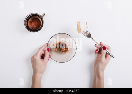 Women's hands with a red manicure pinned on a fork piece of cake, top view Stock Photo