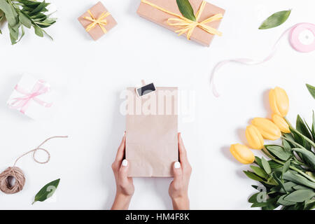 Top view of a female hand holding a paper bag with a gift on a table near the tulips, ribbons and boxes Stock Photo