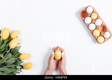 Top view of female hands holding yellow Easter egg near tulips on white background Stock Photo