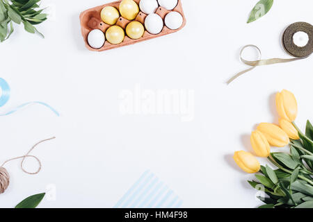 Frame of Easter eggs, yellow flowers, boxes of gifts and ribbons, top view Stock Photo