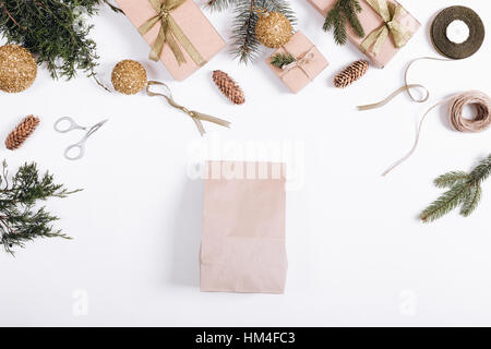 Festive composition: boxes with gifts, ribbons, paper bag, Christmas tree branches and cones, rope, scissors. Top view, white background. Stock Photo