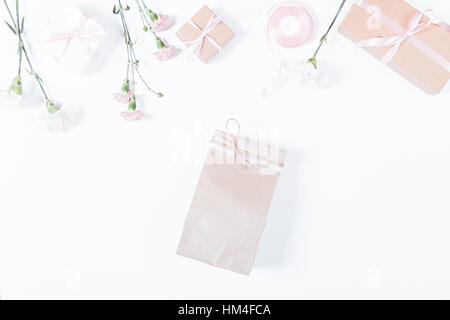 Paper bag, flowers, boxes with gifts and ribbons on white table, top view, space for text Stock Photo
