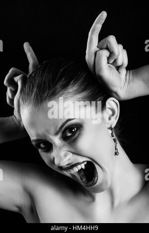 fun luxury woman vampire making devil horns screaming on black background monochrome Stock Photo