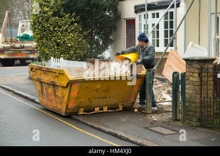 Builders waste rubbish skip, on pavement & yellow, line being filled / loaded builder loading while skips lorry waits. UK Stock Photo