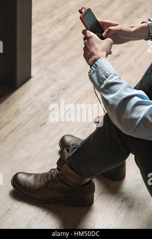 Young man sitting on floor and using phone Stock Photo