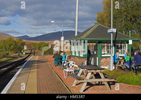People sitting outside at picnic tables on the platform at Rannoch Railway Station, having refreshments, on a sunny autumn afternoon.  Perthshire. Stock Photo