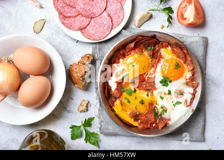 Fried eggs with salami, bacon and tomatoes, top view Stock Photo