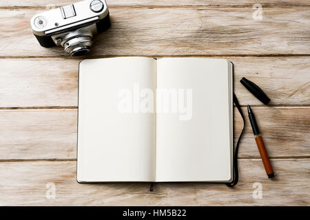 high-angle shot of an open notebook with a blank space, a pen and an old film camera on a white rustic wooden table Stock Photo