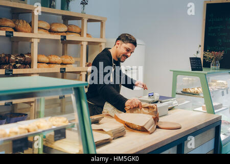 Happy owner holding paper bag while standing at counter in bakery Stock Photo