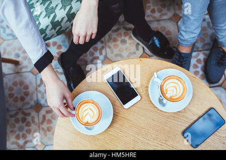 Low section of businesswomen with coffee and mobile phones on table in cafe Stock Photo