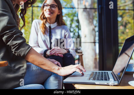 Midsection of woman using laptop computer while sitting with colleague in cafe Stock Photo
