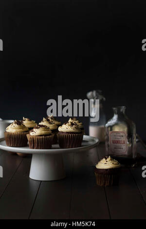 Cupcakes in cakestand with bottles on table against black background Stock Photo