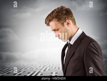 Thoughtful business man looking down with maze in background Stock Photo