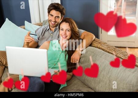 Composite image of hanging red hearts and couple doing online shopping Stock Photo
