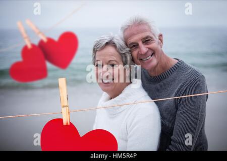 Composite image of hanging hearts and senior couple embracing on beach Stock Photo