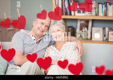 Composite image of red heart and senior couple embracing on sofa Stock Photo
