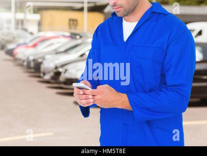 Car mechanic using mobile phone against car parked Stock Photo