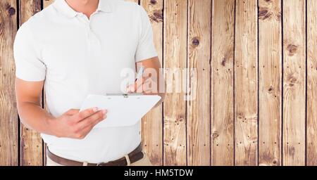 Delivery man writing on clipboard against wooden background Stock Photo