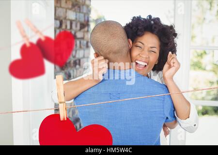 Composite image of red hanging hearts and excited couple embracing Stock Photo