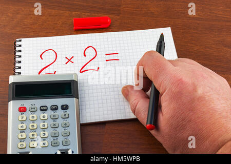 On the notebook sheet in a cage man's hand writes the equation Stock Photo