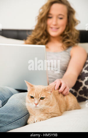 Teenage girl (16-17) lying on bed with laptop and stroking ginger tabby cat Stock Photo