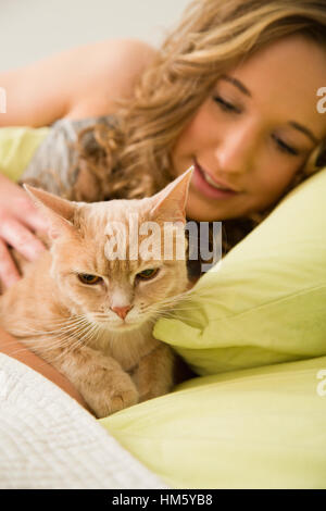 Teenage girl (16-17) lying in bed and stroking ginger tabby cat Stock Photo