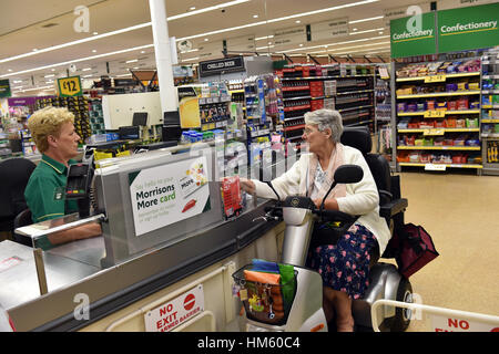 A disabled woman is helped at the supermarket checkout with her shopping while using her mobility scooter. Stock Photo