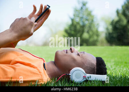 Young man lying on grass, listening to music Stock Photo